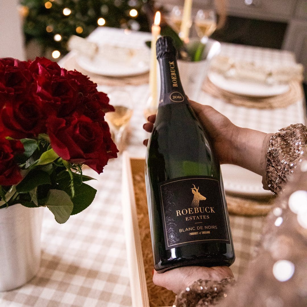 Person holding a bottle of Roebuck Blanc de noirs against a Christmas decorated table.